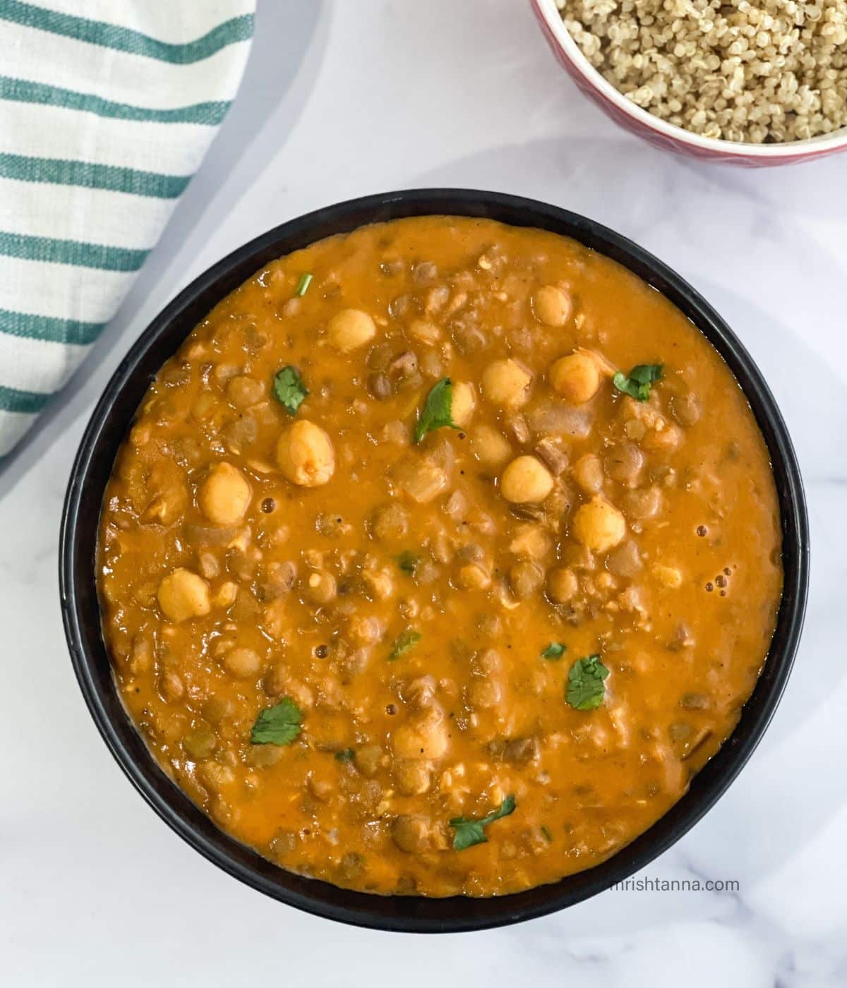 A bowl of chickpea and lentil curry is on the white surface.