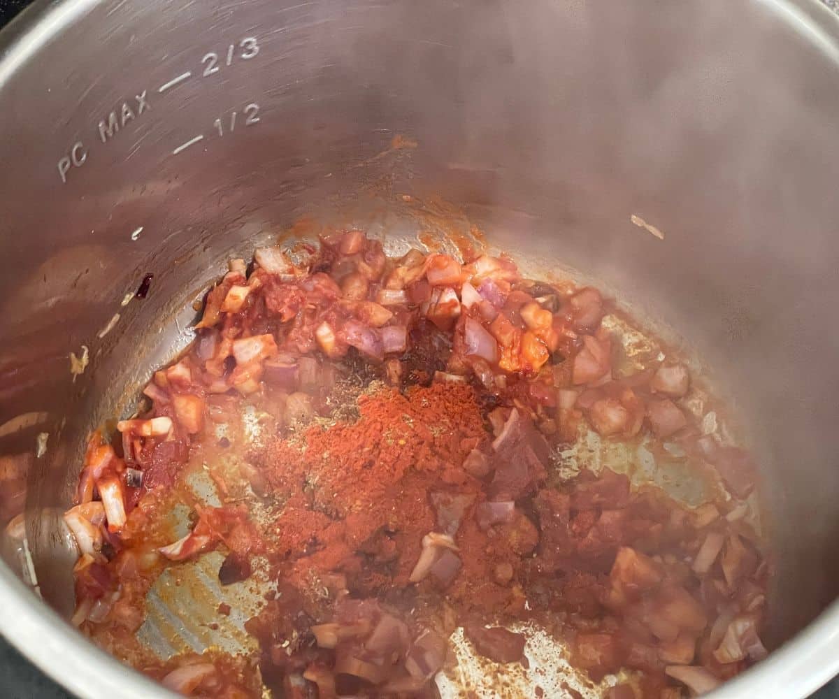 An instant pot has spices and tomato paste.