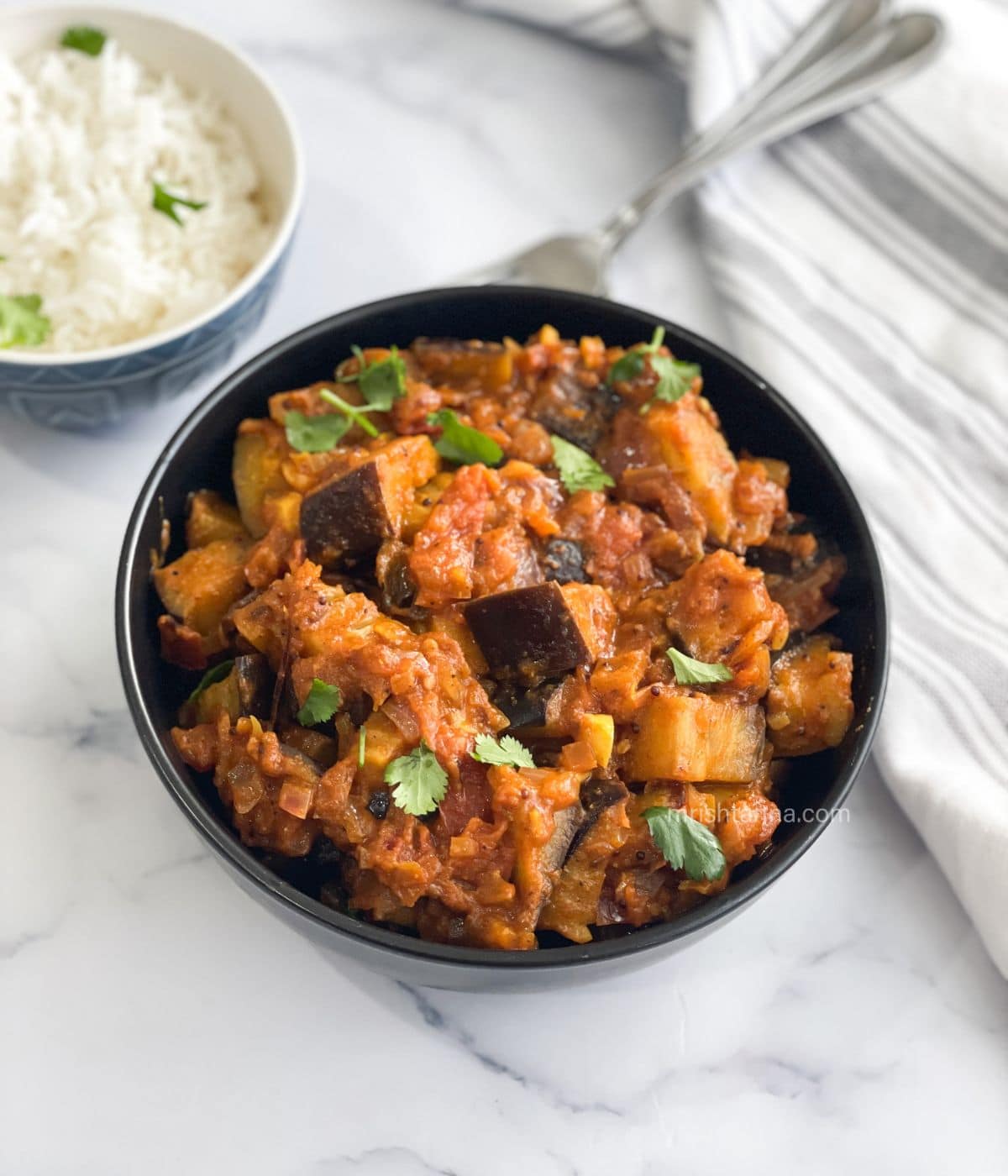 A bowl of brinjal masala is on the table.