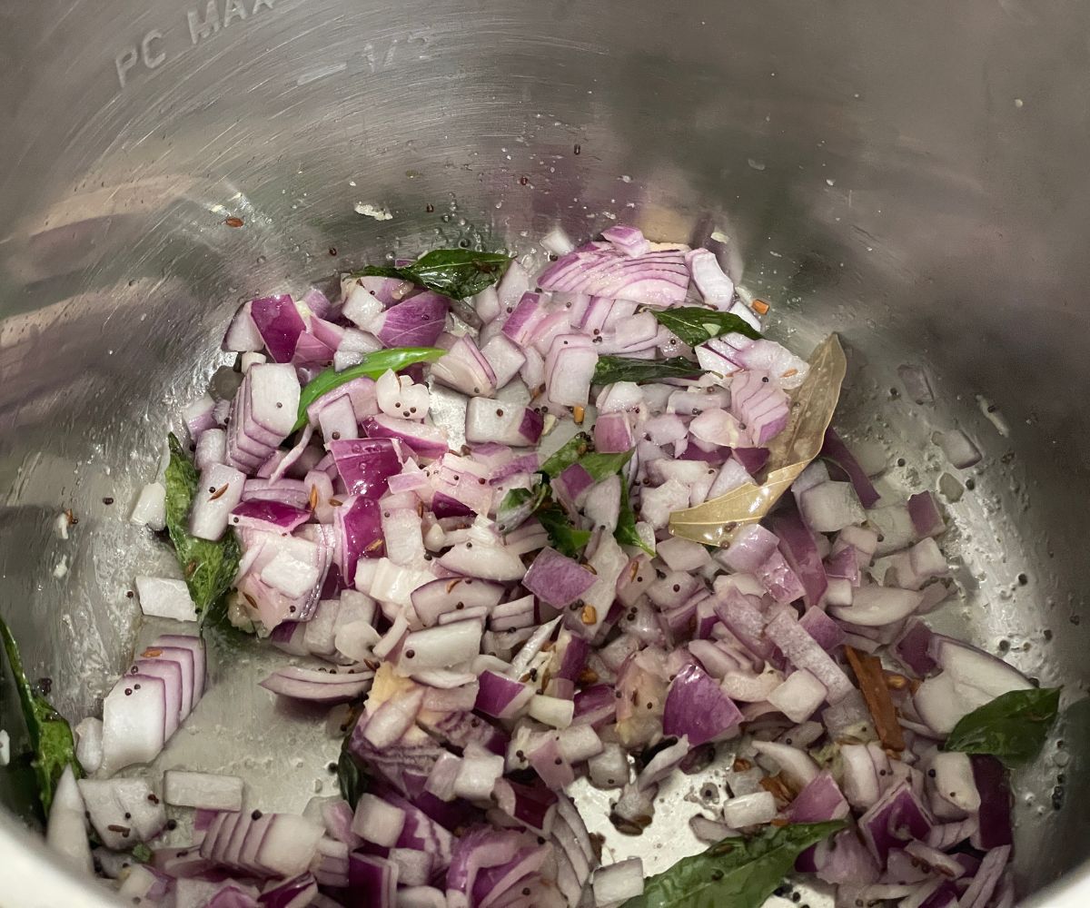 An instant pot has chopped onions and spices.