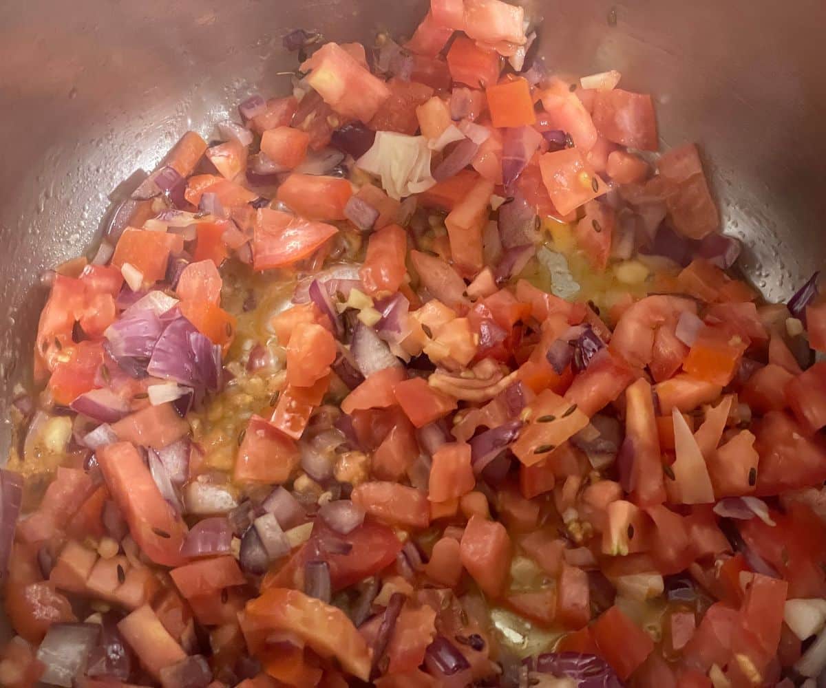 An instant pot has onions, tomatoes and other spices.