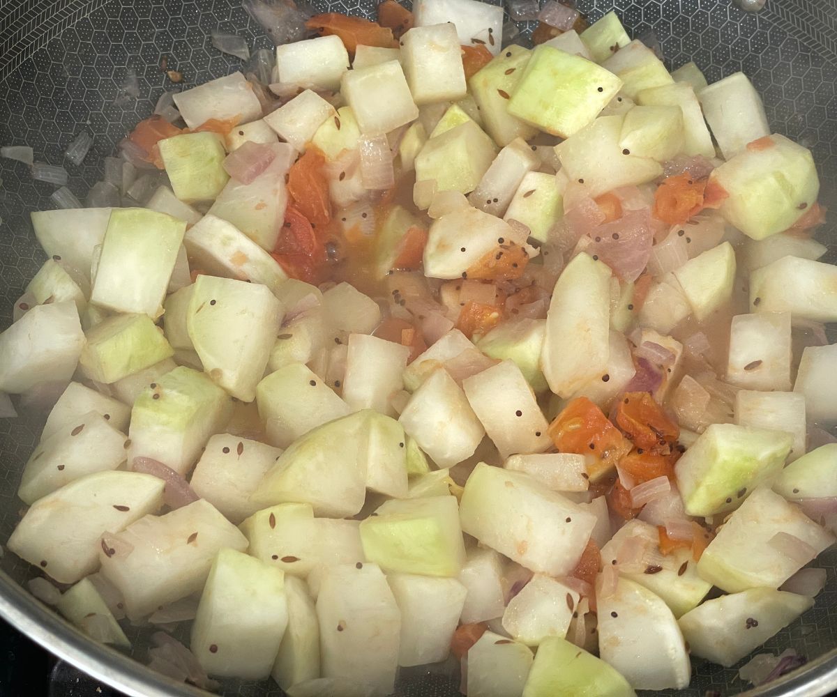 A pan has kohlrabi and spices over the heat.