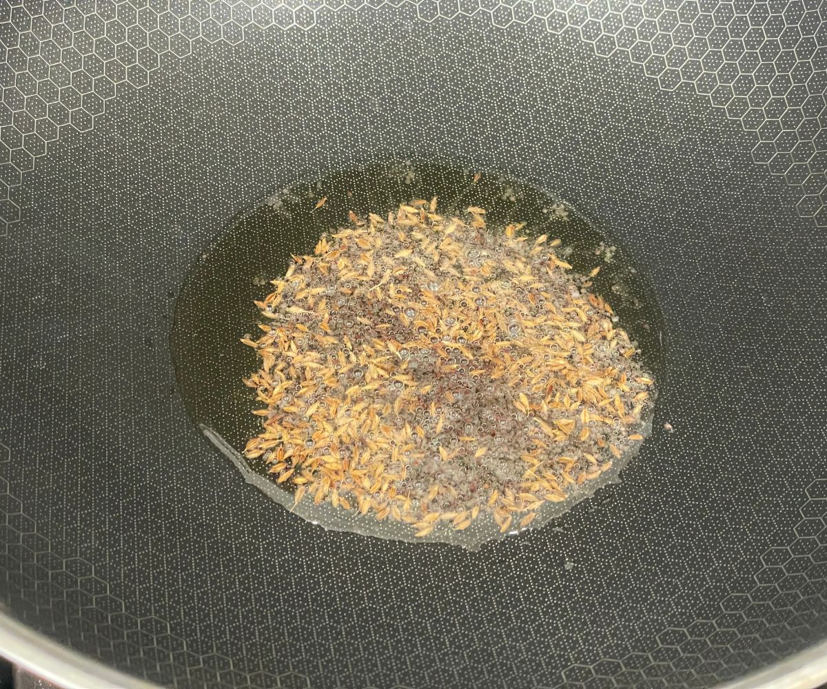 A pan has heated oil and mustard and cumin seeds.