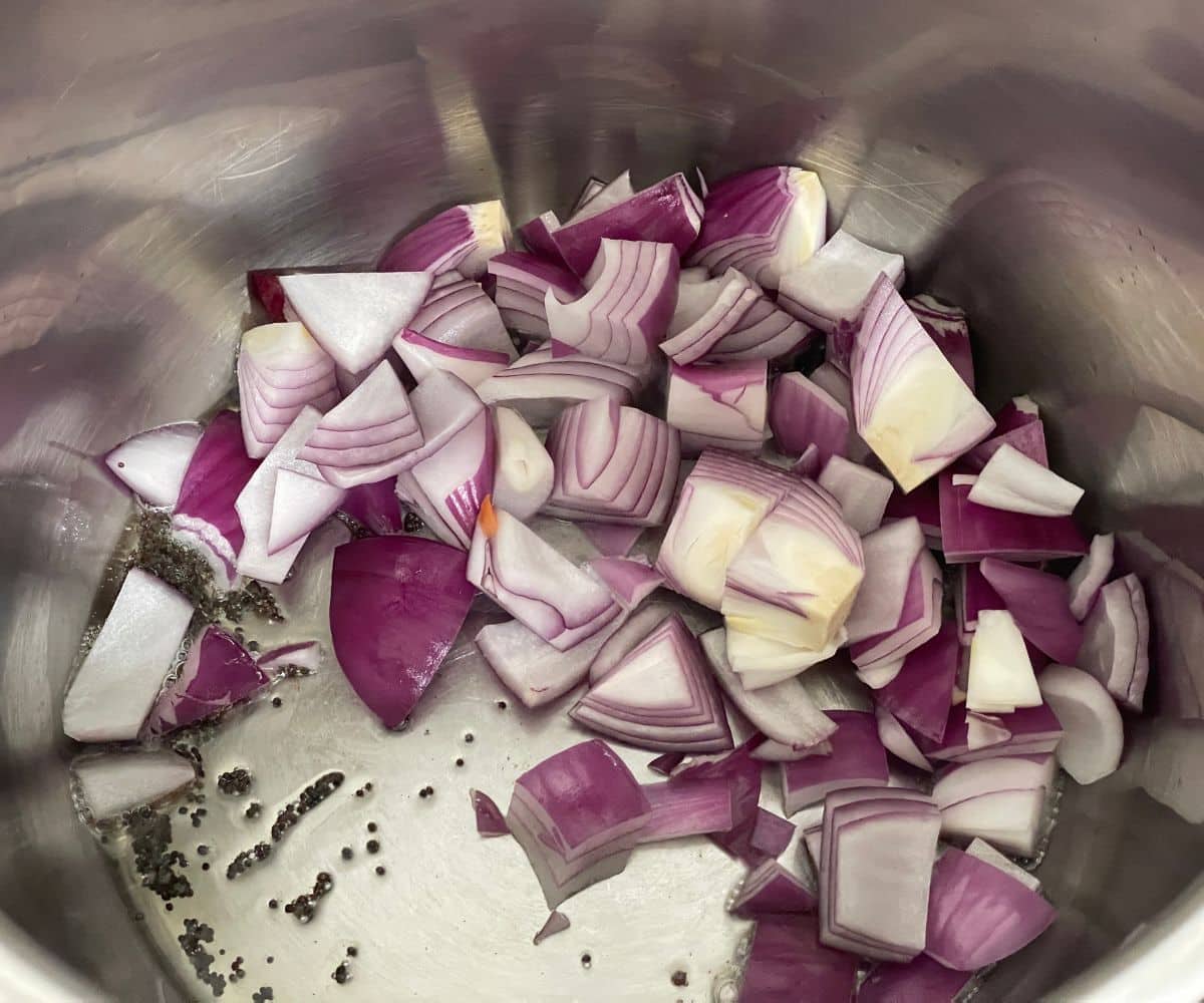 An instant pot has spices and chopped onions, garlic and ginger.