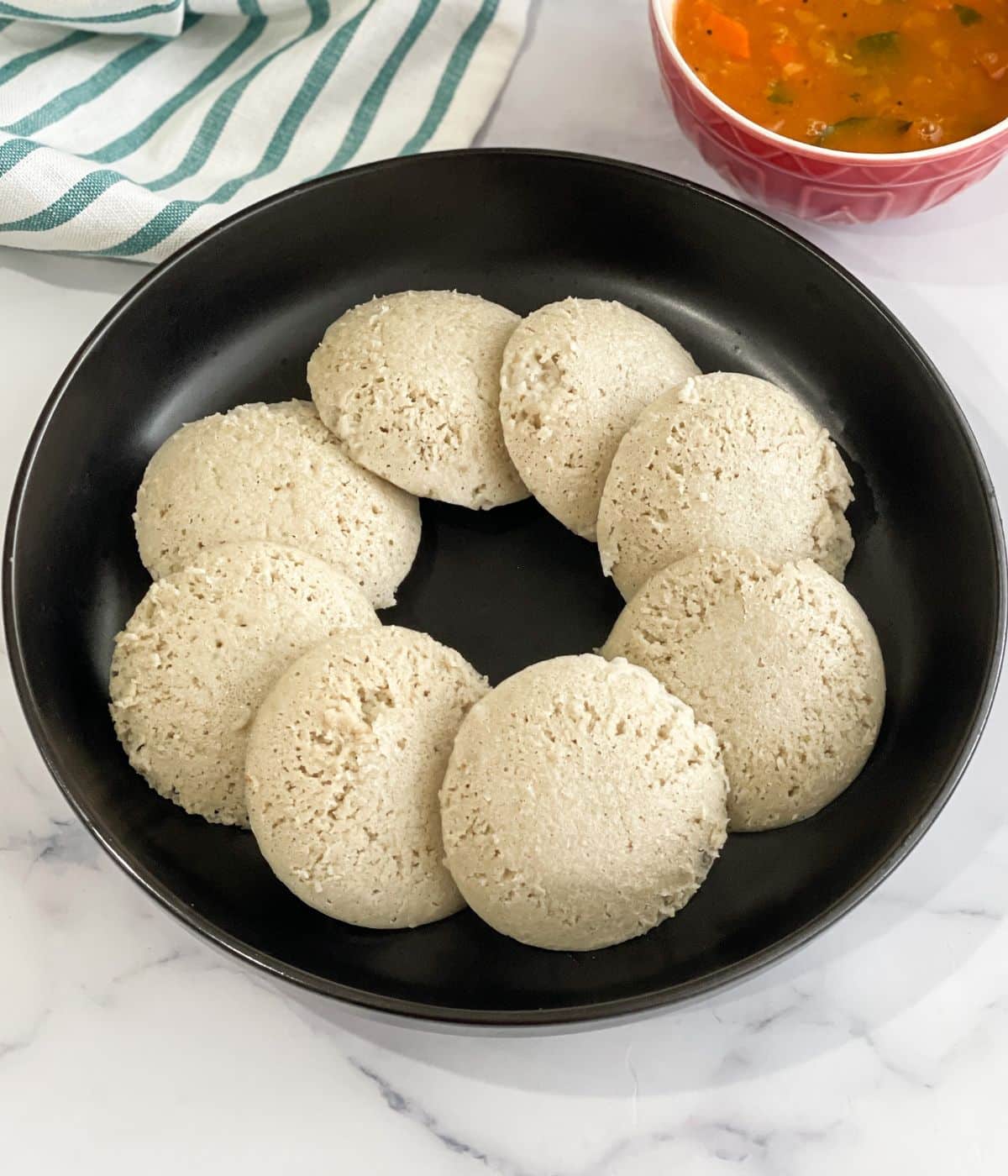 A plate has quinoa idlis and a  bowl of sambar by the side.