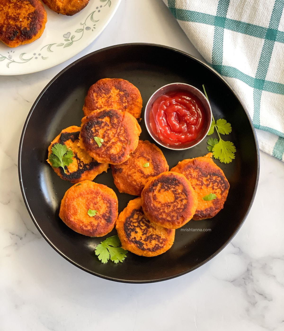 A plate has sweet potato tikkis and bowl of ketchup.