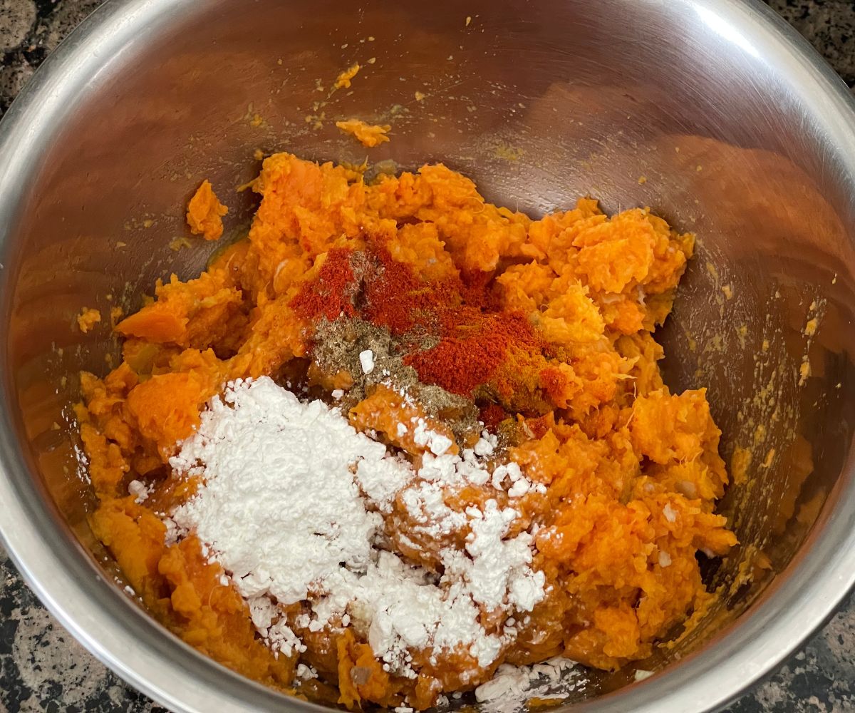 A bowl has mashed sweet potatoes and other ingredients for tikki.