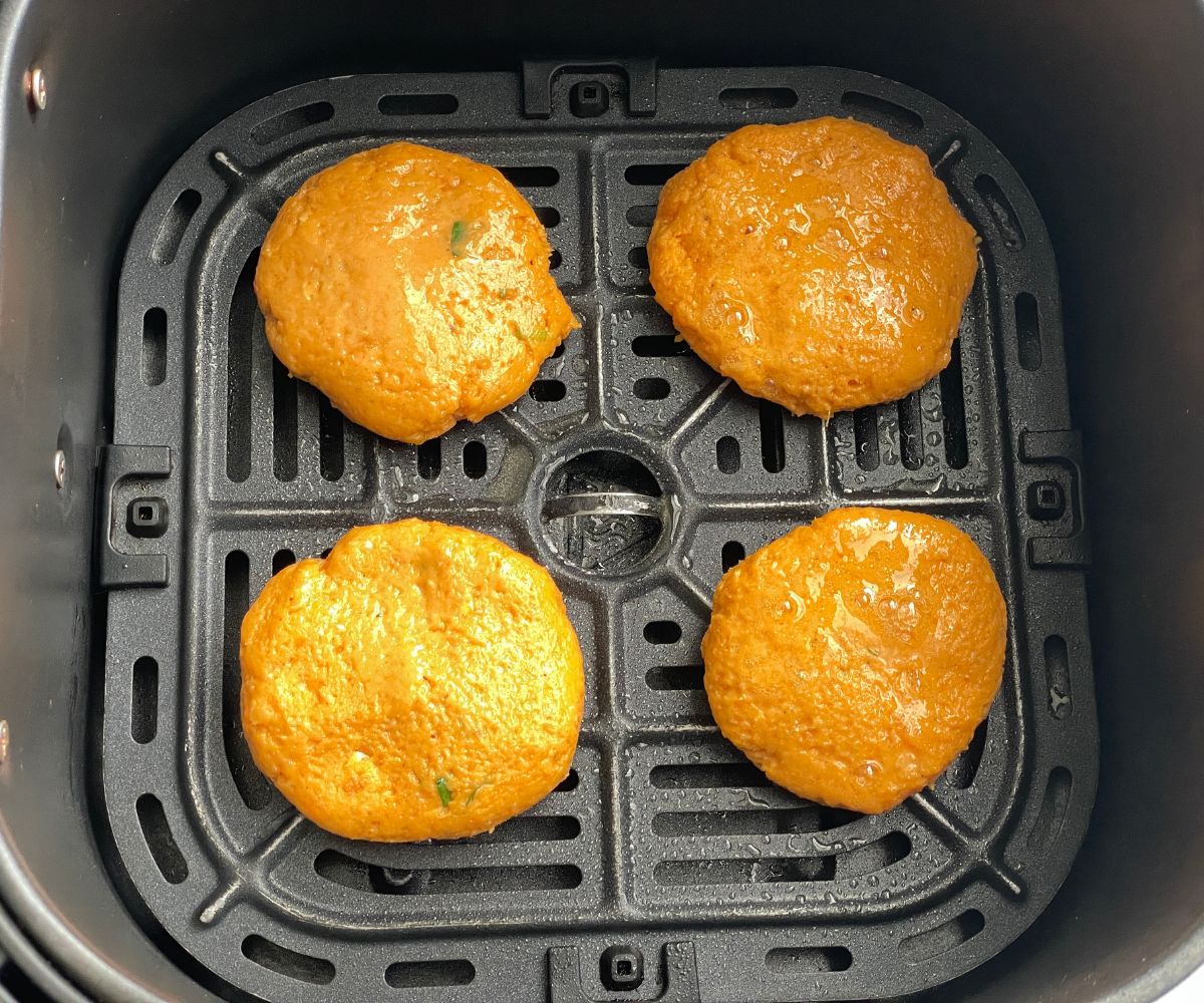 Air fryer basket has sweet potato patties.