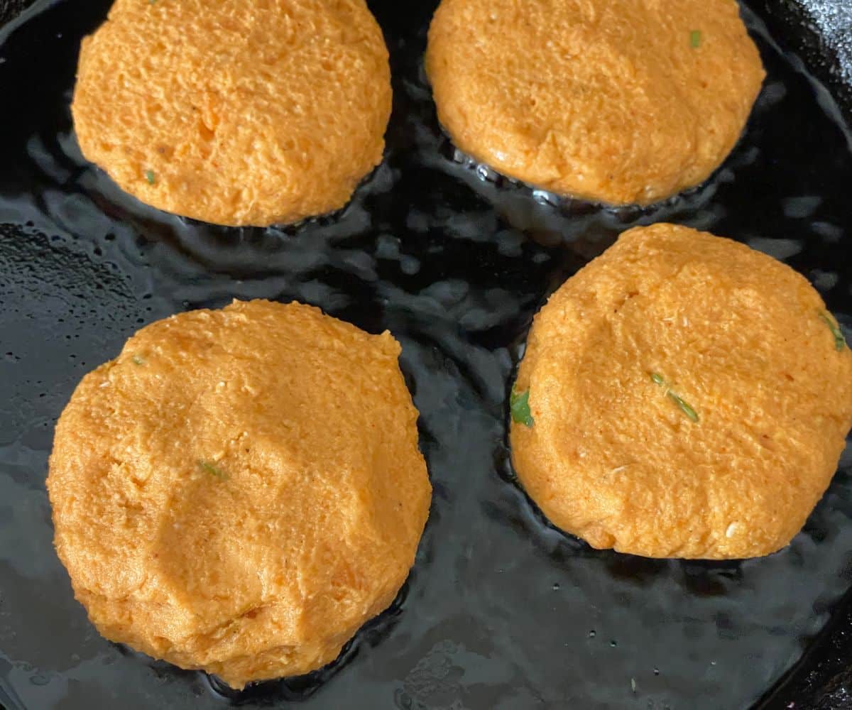 A heated pan has oil and sweet potato cutlets.