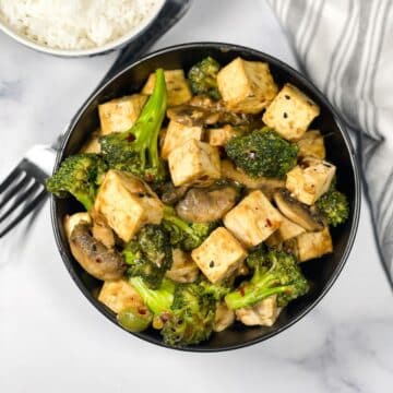 A bowl of tofu broccoli mushroom stir fry is on the table.