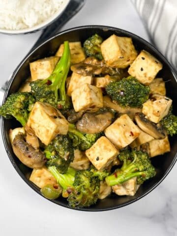 A bowl of tofu broccoli mushroom stir fry is on the table.