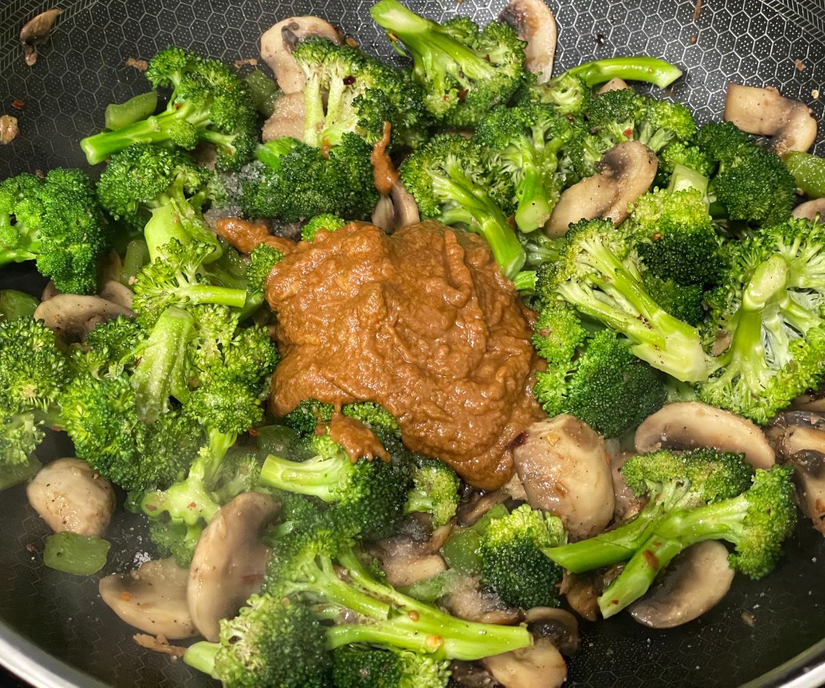A wok has veggies and butternut butter sauce mix.