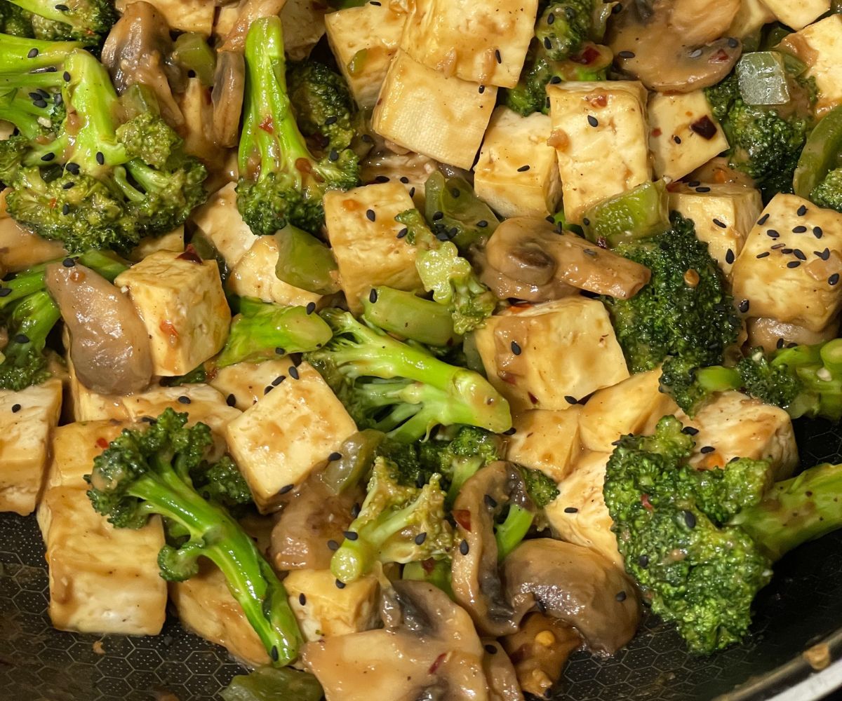 A pot has stir fried tofu, broccoli and mushrooms.
