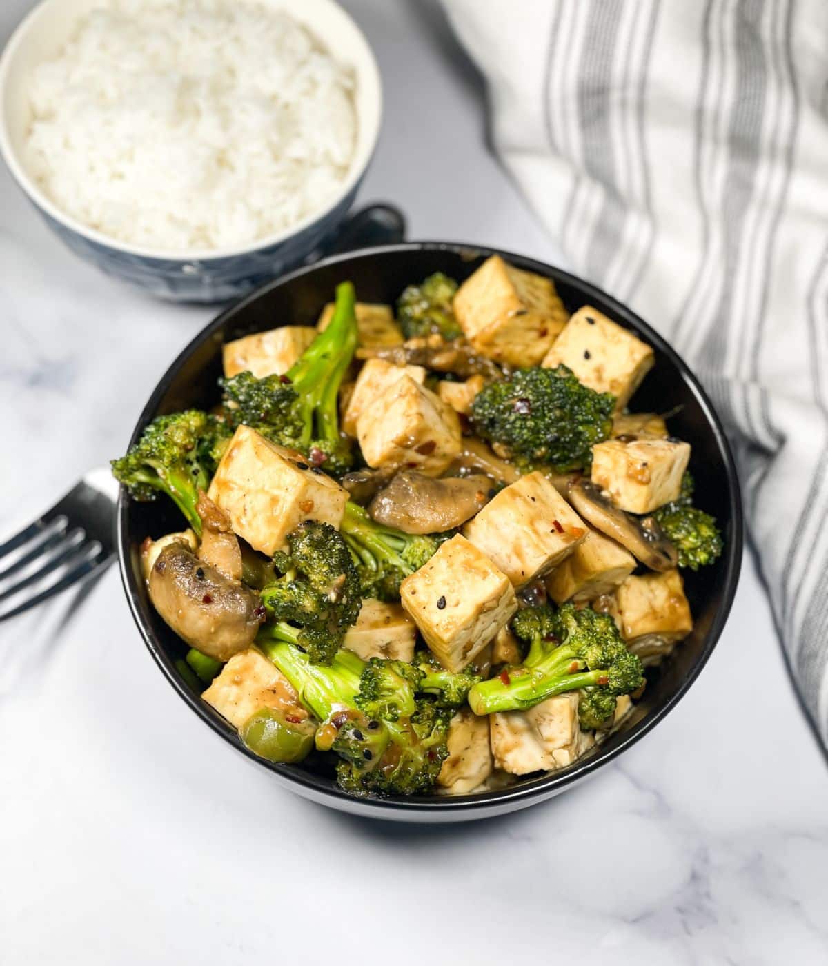 A bowl is full of stir fried tofu broccoli and mushroom recipe.