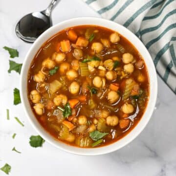 A bowl has garbanzo bean soup and topped with cilantro.