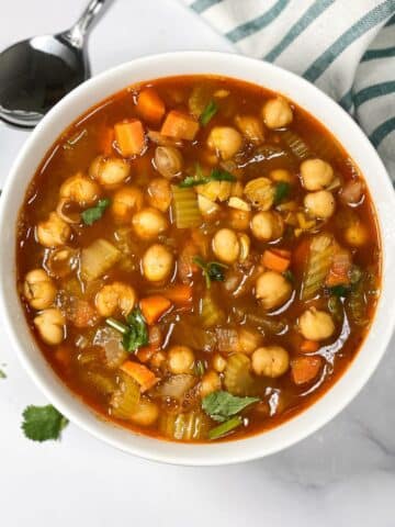 A bowl has garbanzo bean soup and topped with cilantro.