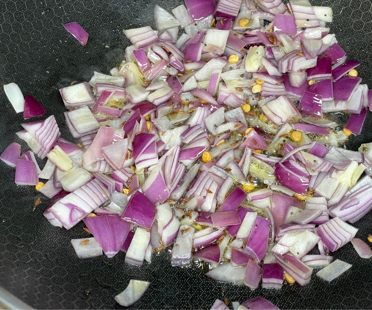 A heated pan has spices and chopped onions.