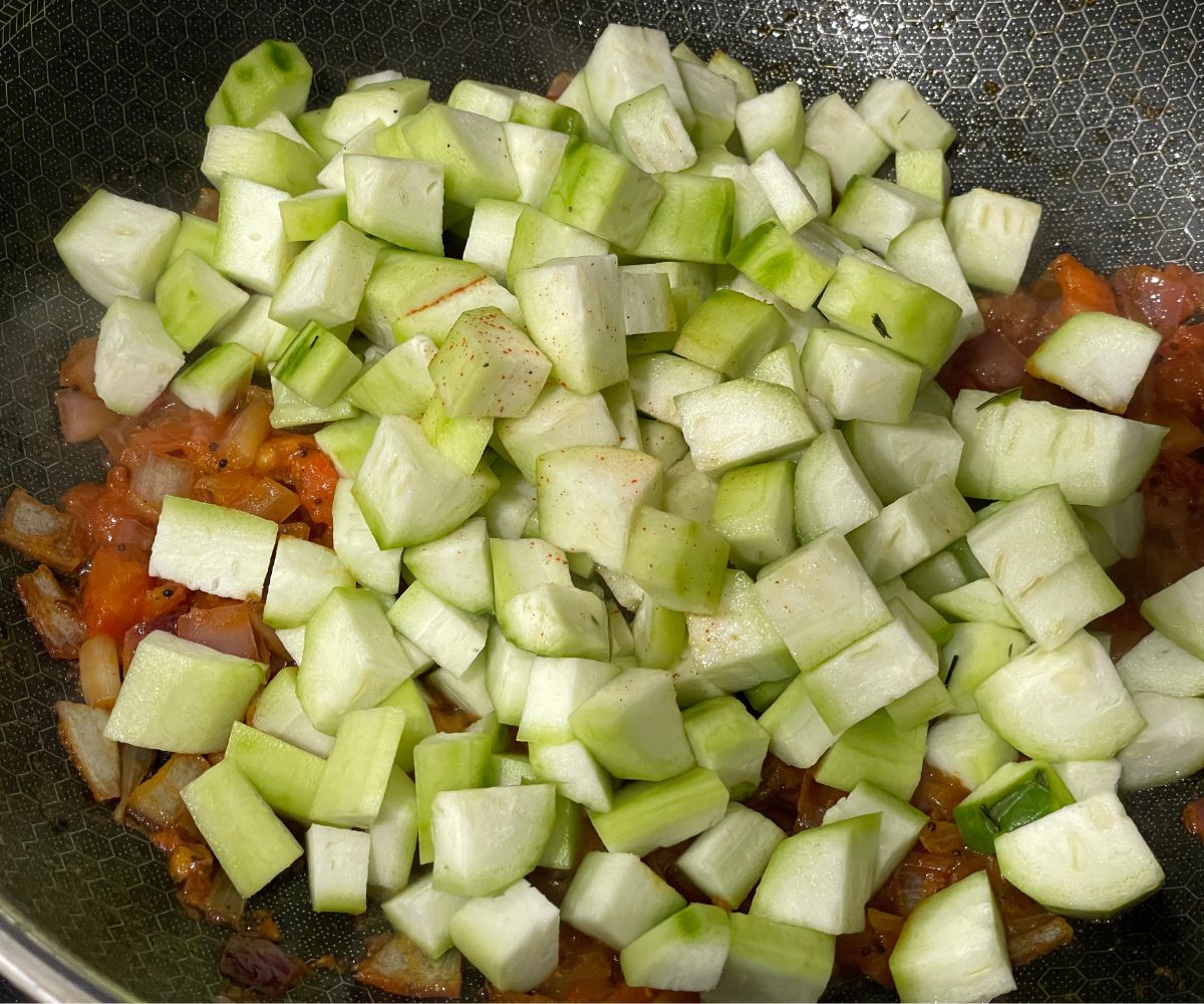 A pan has all the spices and chopped ridge gourds.
