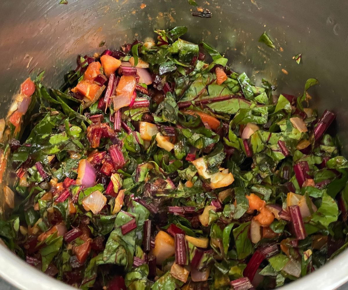 An instant pot has chopped beet greens and tomatoes.