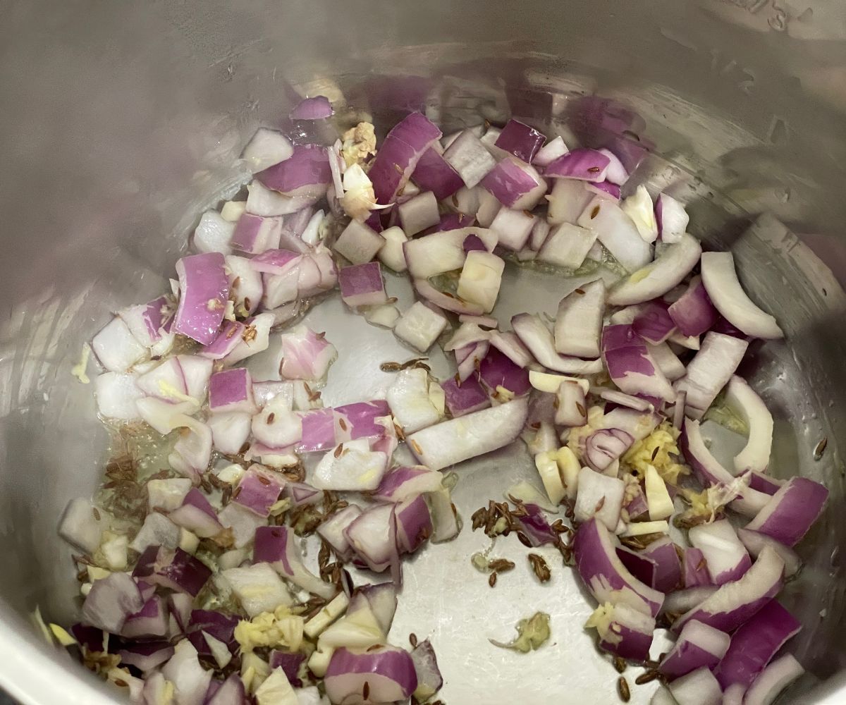 An instant pot has spices and chopped onions.