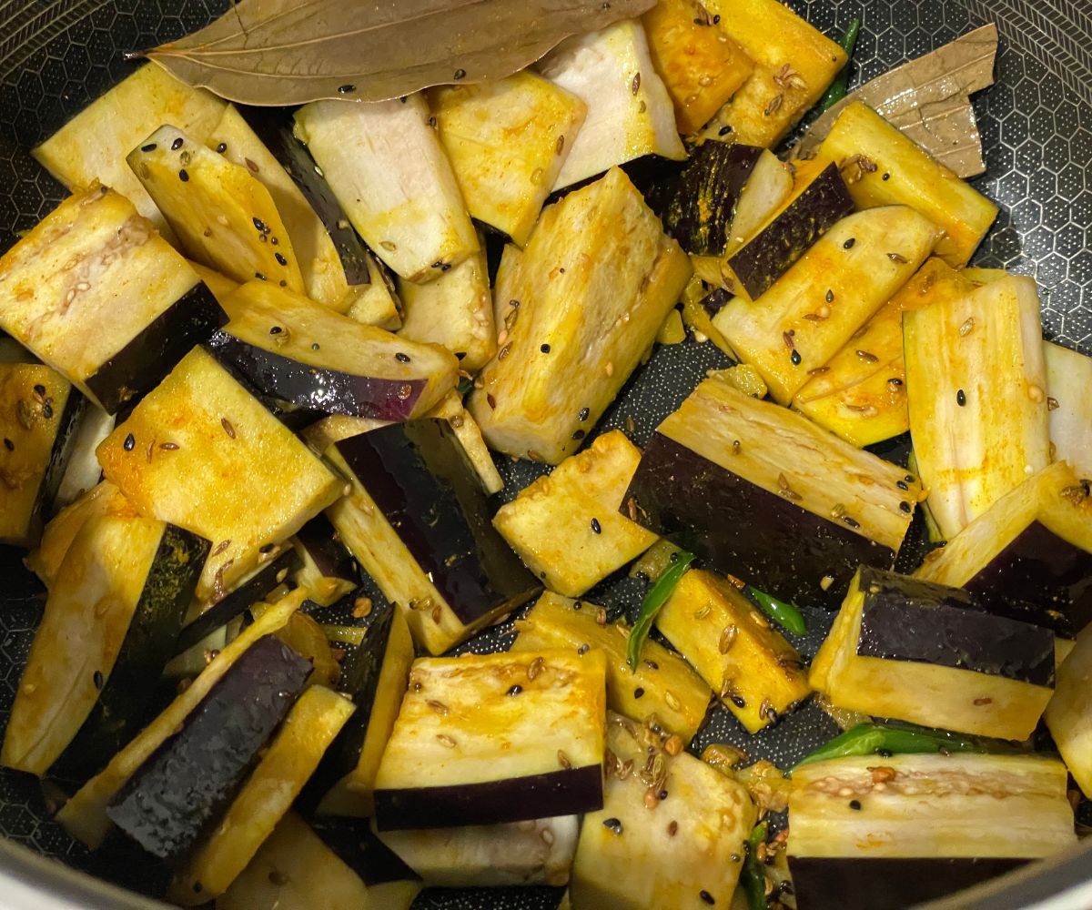 A pot has eggplants along with spices over the heat.