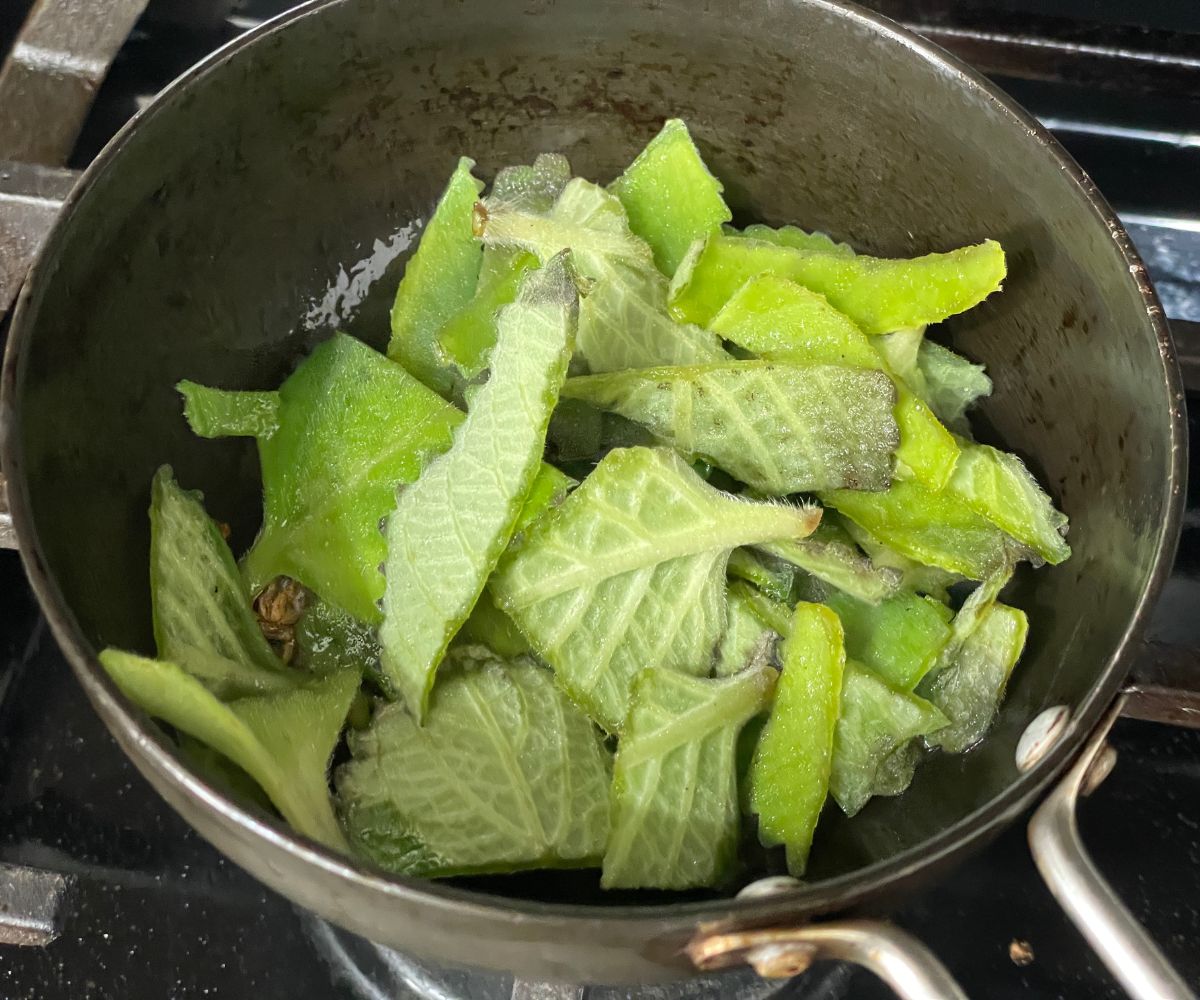 A pan has spices and Indian borage leaves over the heat.