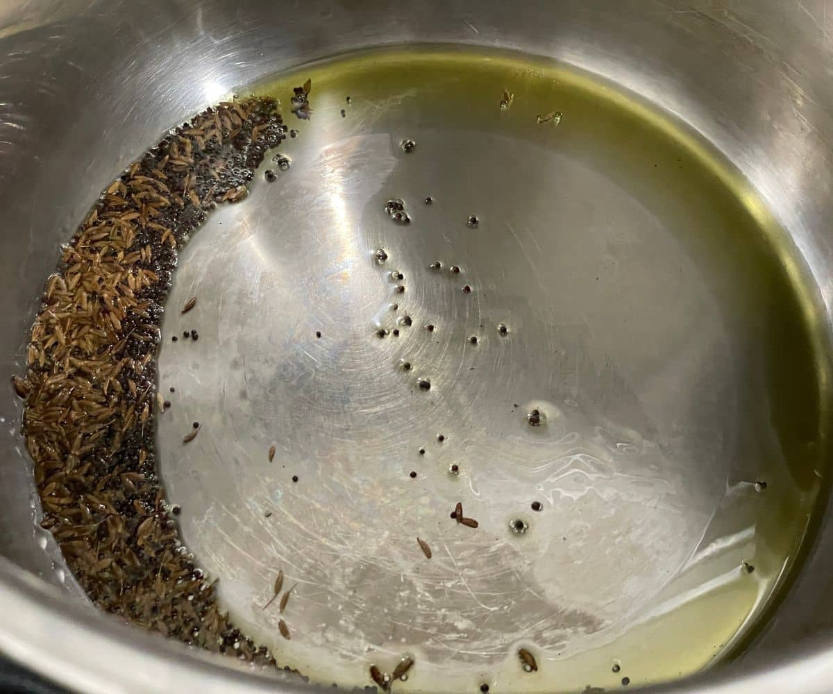 An instant pot has oil, and spices on saute mode.