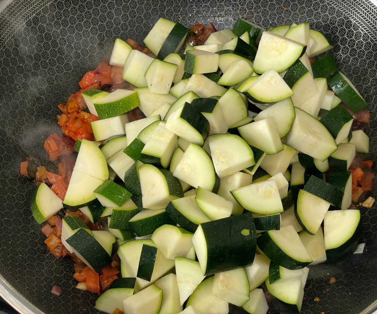 A pan has all the ingredients along with zucchini cubes.