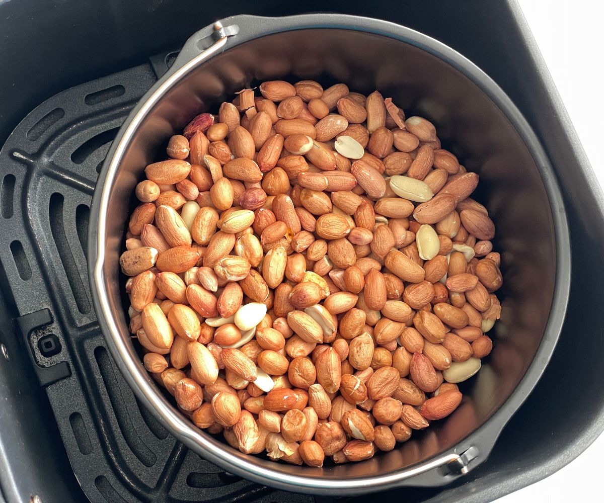 Air fryer basket has raw peanuts.