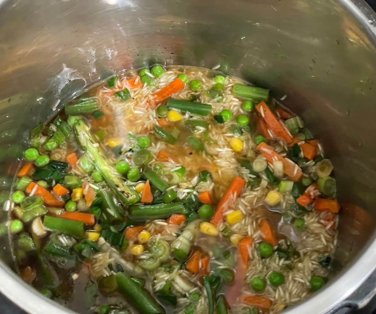 An instant pot has rice and mixed vegetables.