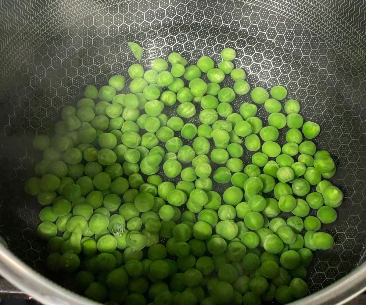 A pan has water and green peas on the stove.