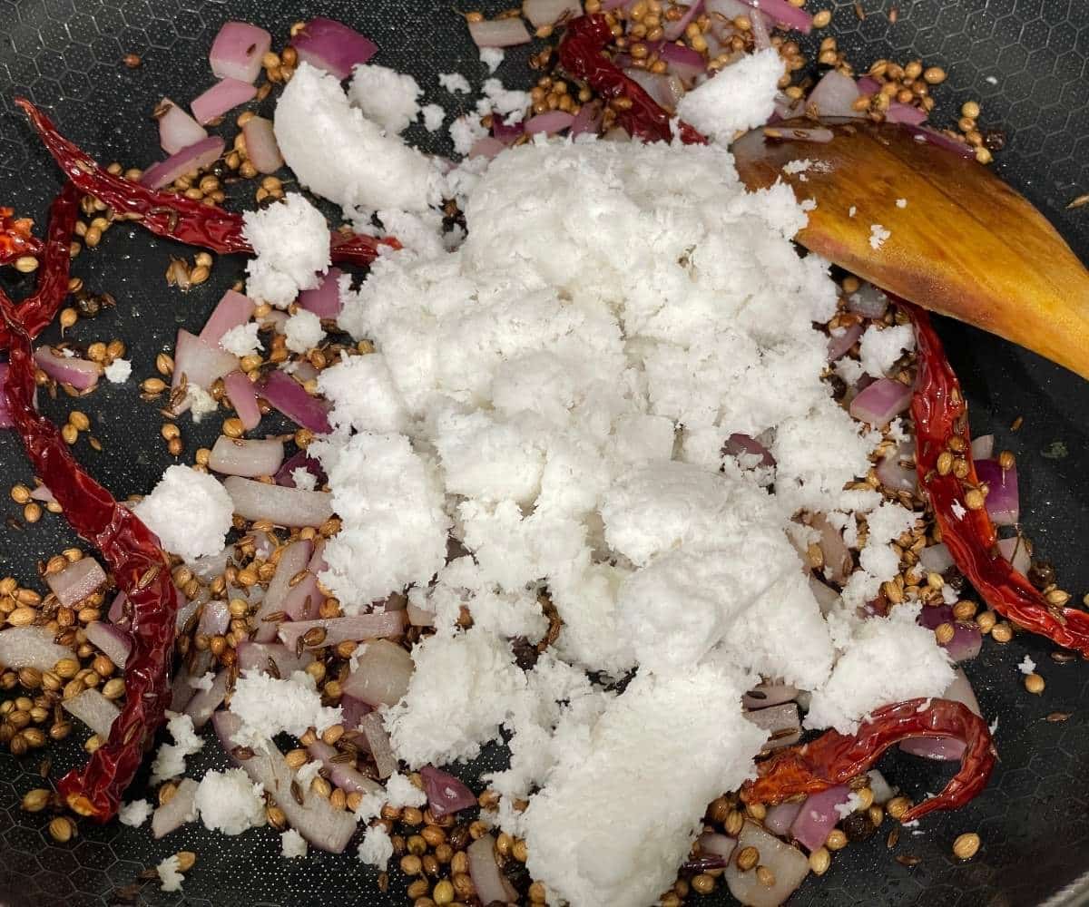 A heated pan is with spices and grated coconuts.