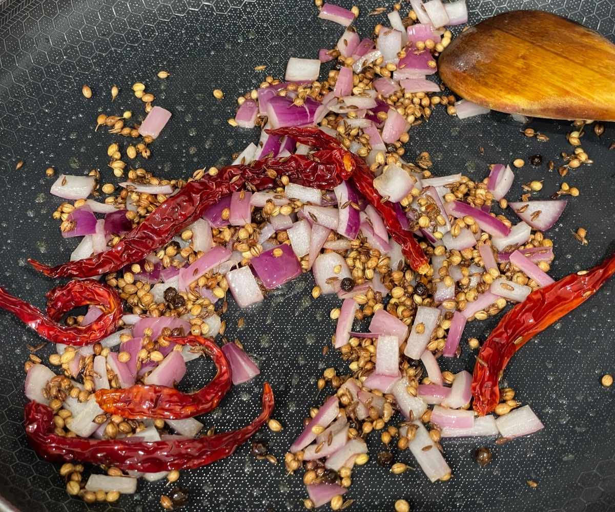 A heated pan is with spices, chilies and onions.