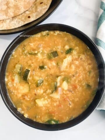 A bowl of zucchini dal is on the surface.