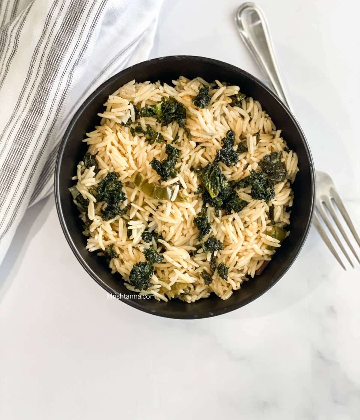 A bowl of kale rice is on the surface with a fork by the side.