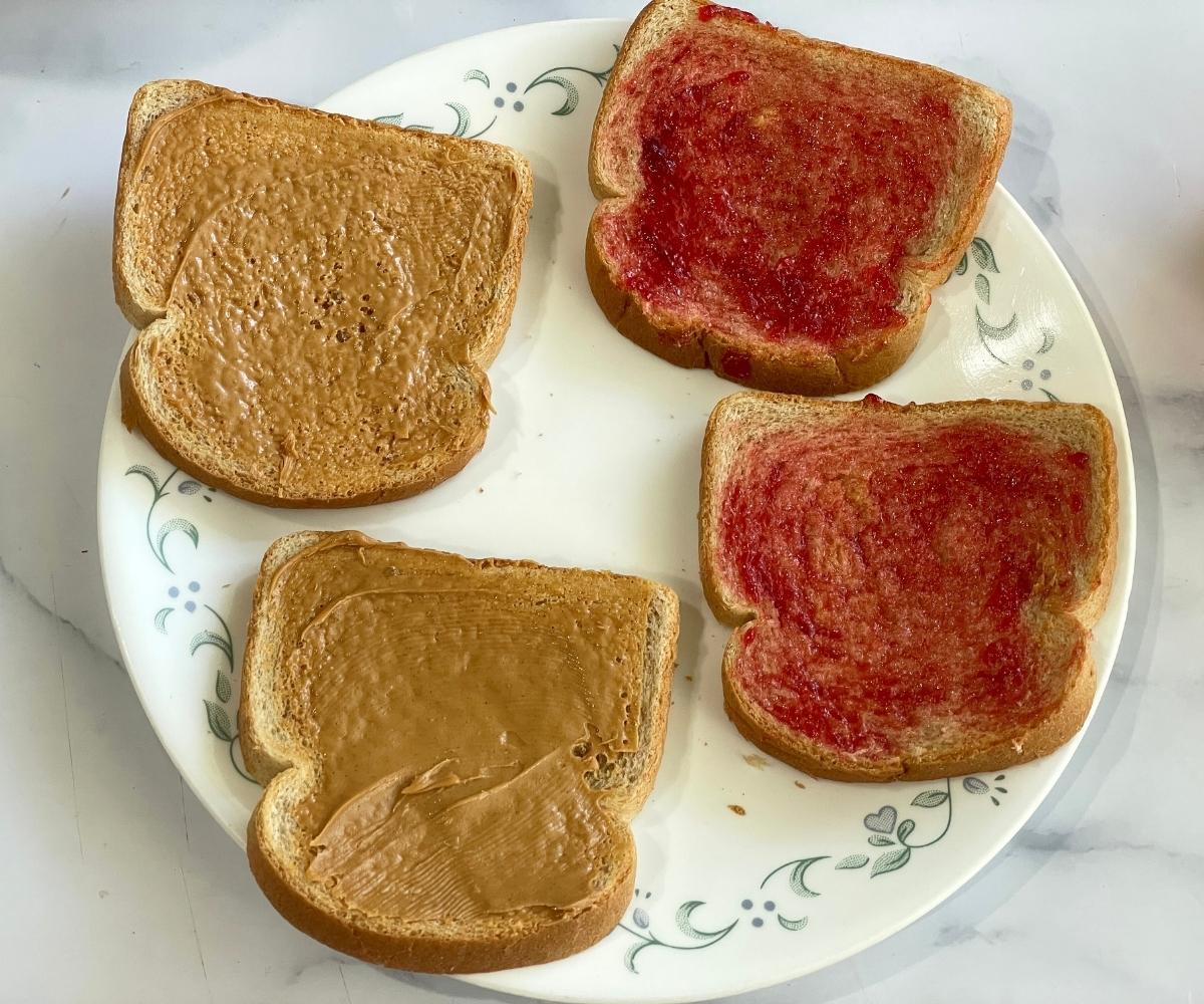 A plate has four pieces of bread topped with peanut butter and jelly.