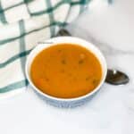 A bowl of lentil soup is on the table with a spoon.
