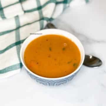 A bowl of lentil soup is on the table with a spoon.