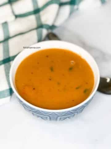 A bowl of lentil soup is on the table with a spoon.