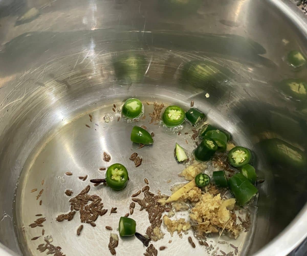 An instant pot has spices and chopped chili and ginger on saute mode.