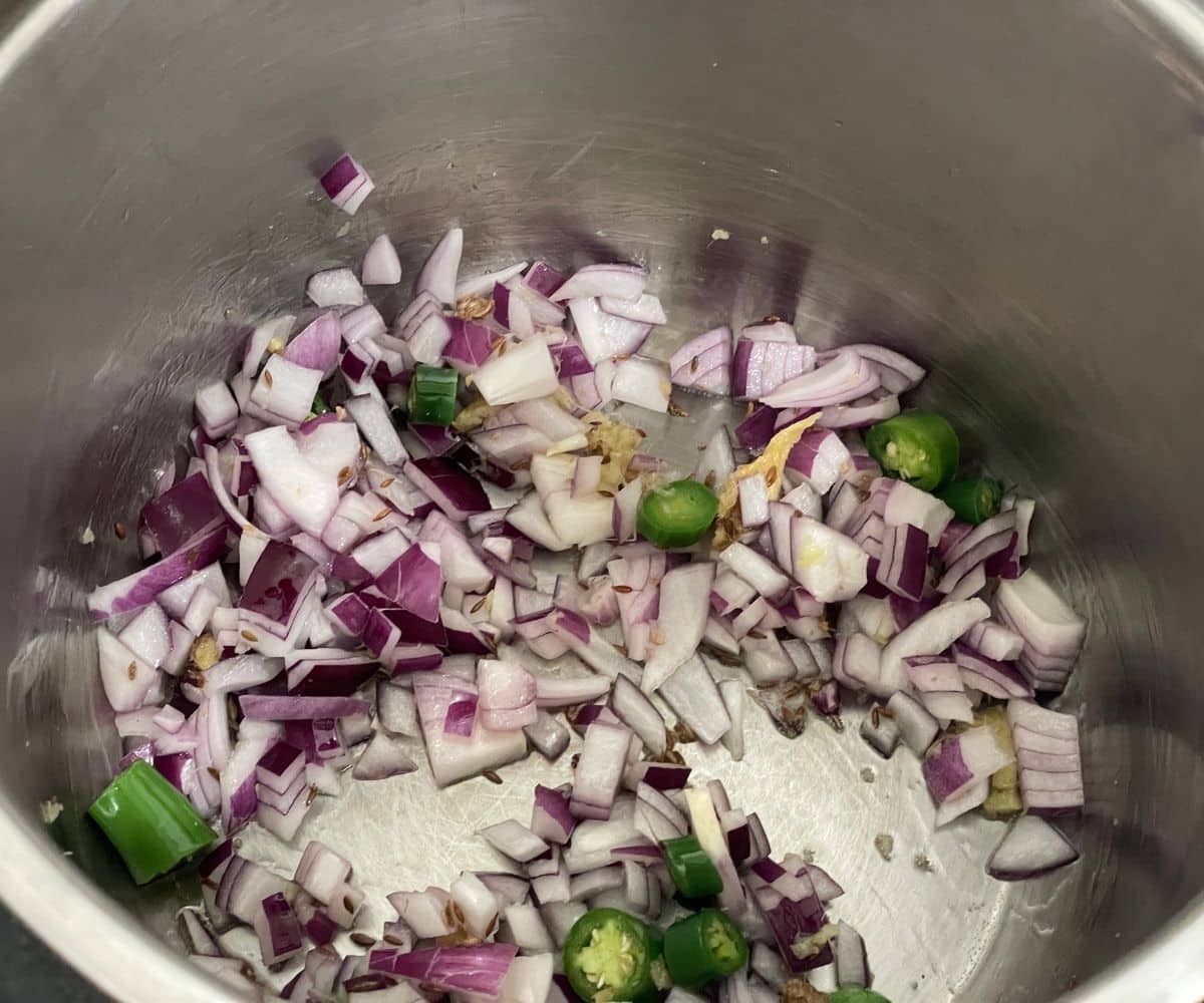 An instant pot has chopped onions and spices.