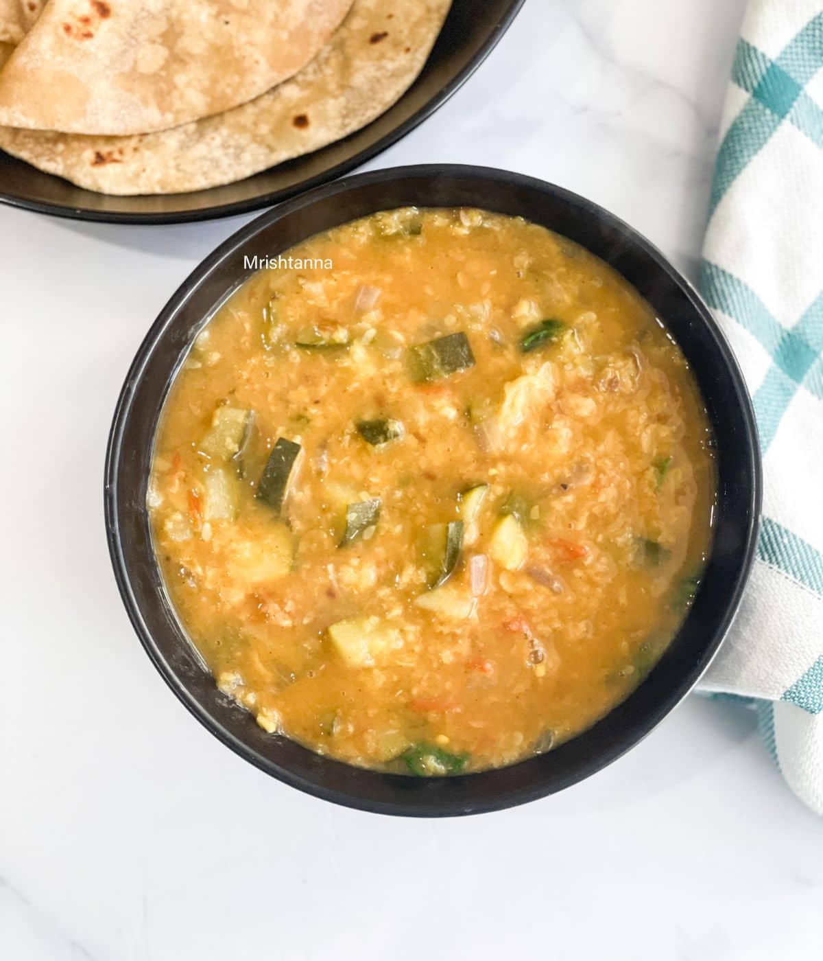 A bowl of zucchini Dal is on the table.