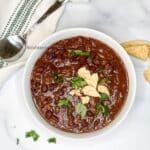 A bowl of black bean chili is on the table with spoon by the side.