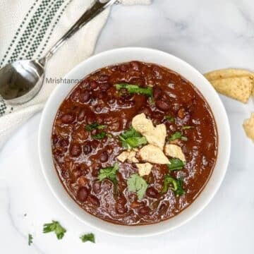 A bowl of black bean chili is on the table with spoon by the side.
