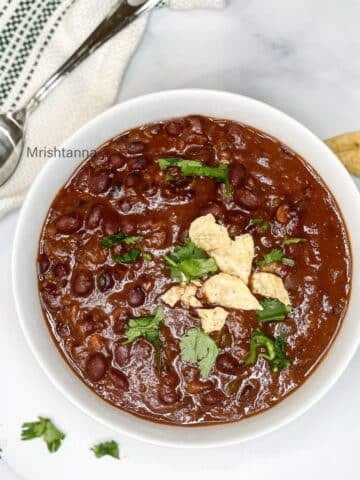 A bowl of black bean chili is on the table with spoon by the side.