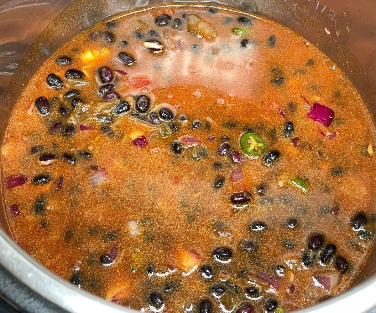 A pot is with black bean chili ingredients in cooking mode.