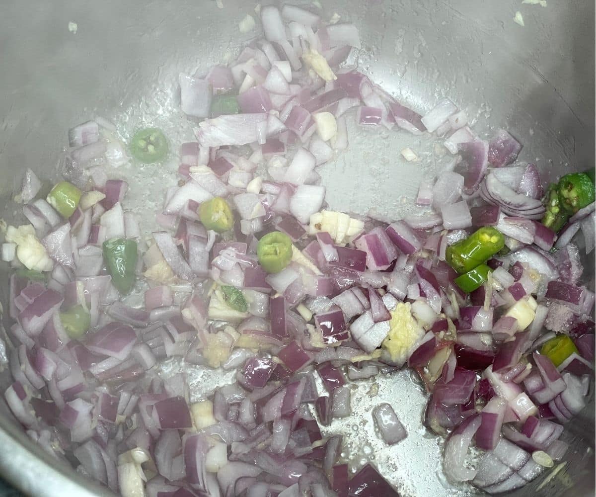 An instant pot is with onions, garlic and other ingredients.