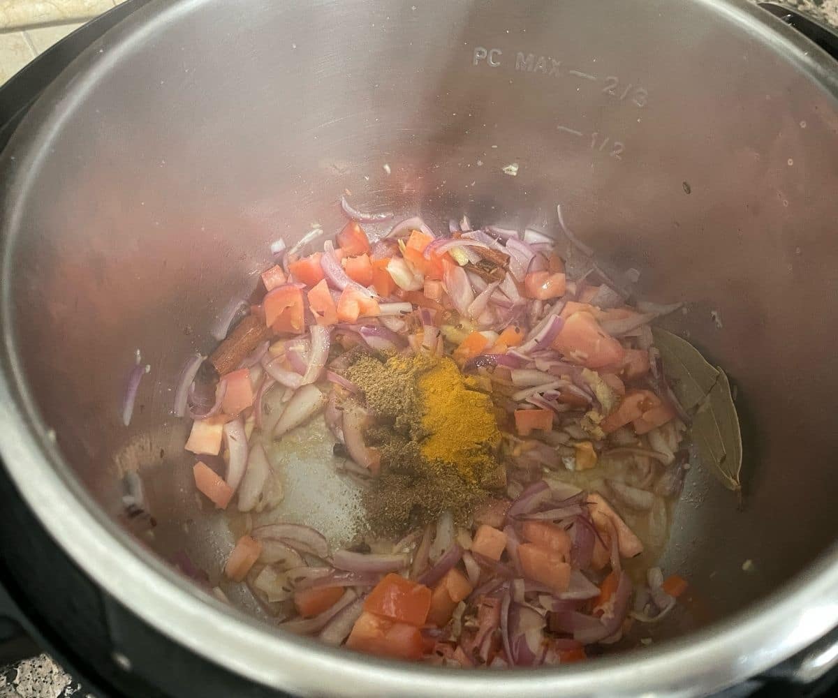 An instant pot has all the spices and tomatoes for the dal pulao recipe.
