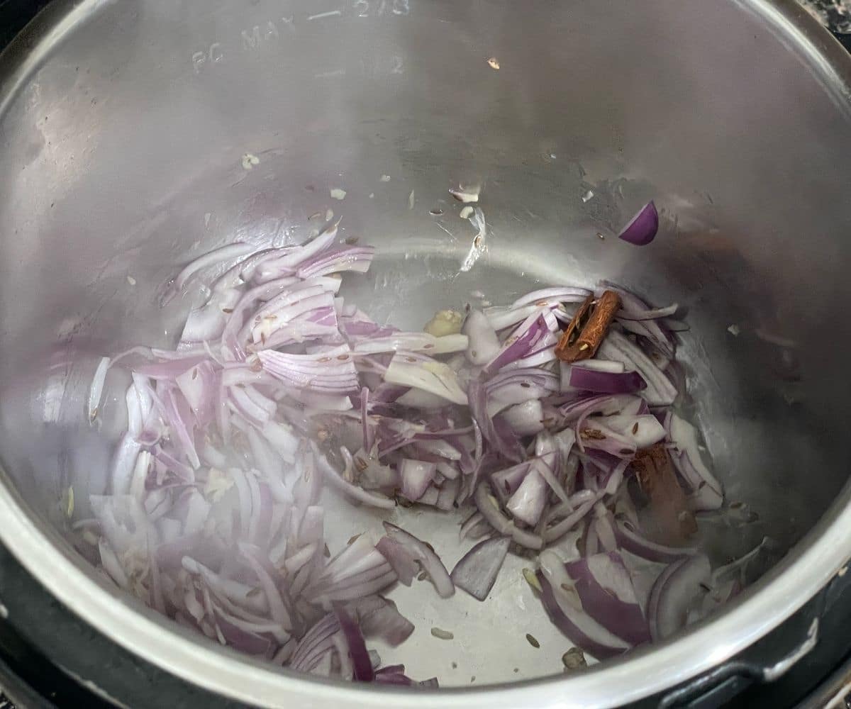 An instant pot is with sliced onions on cooking mode.