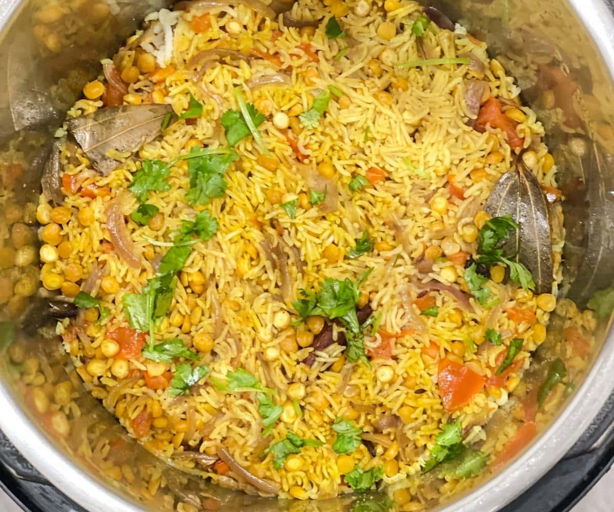 An instant pot has cooked Chana dal pulao topped with coriander leaves.